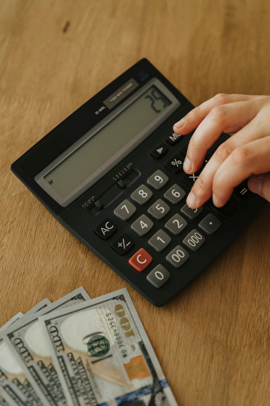 A hand counting banknotes with a calculator