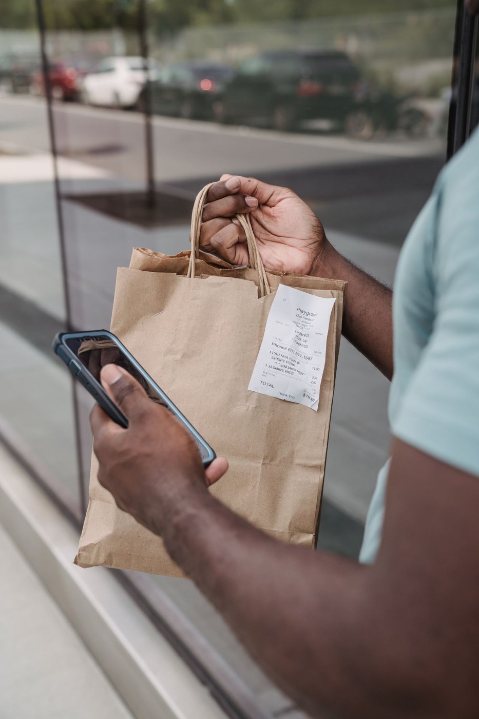 A shopper holding a bag and a receipt beside a phone