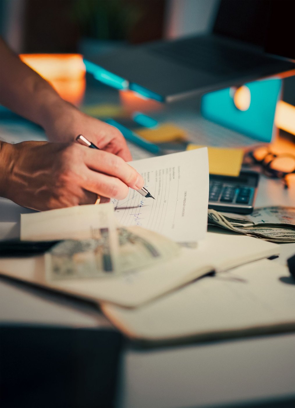 A pen over financial paperwork beside cash and calculator