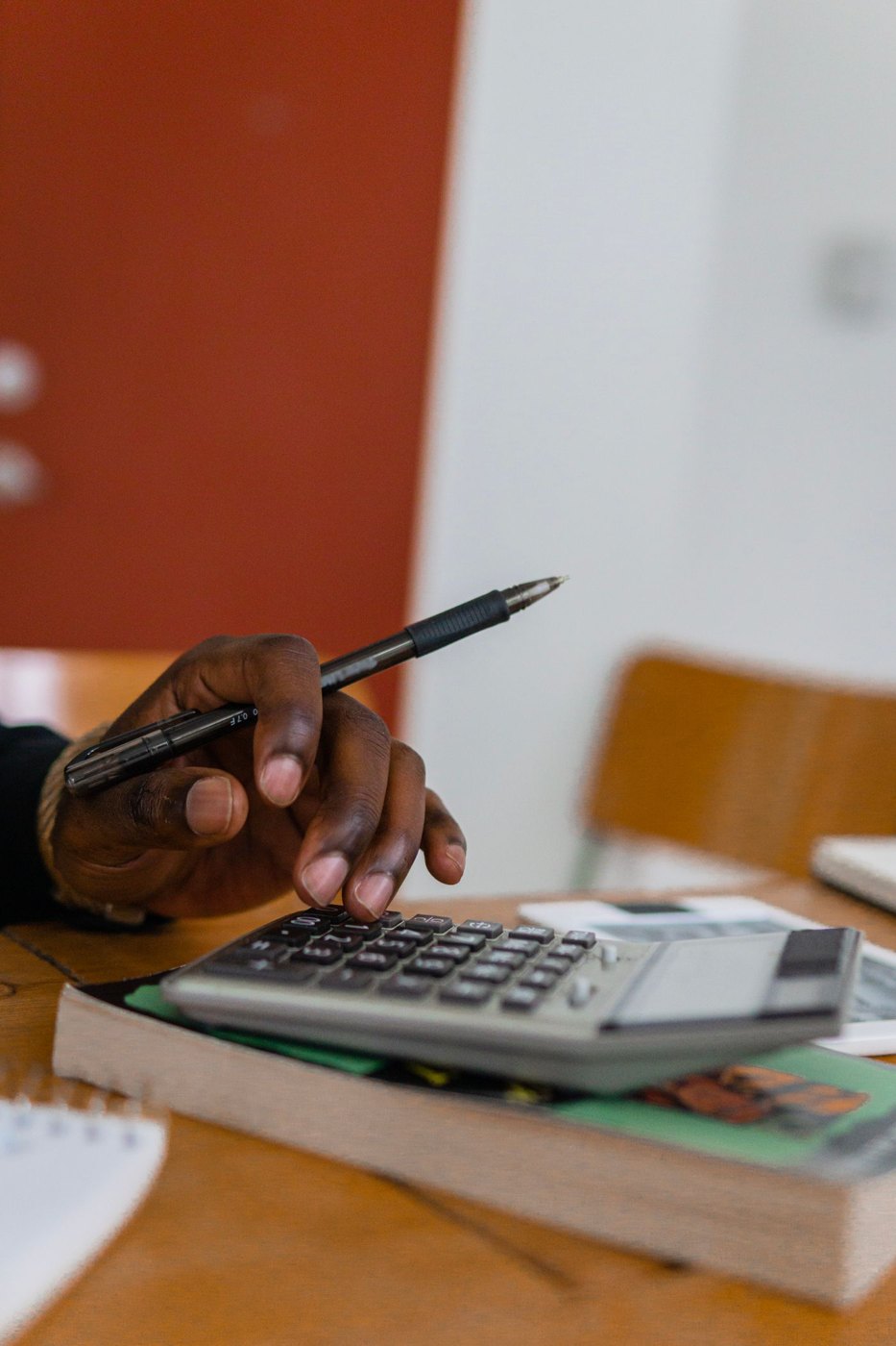 A hand checking calculations beside paperwork